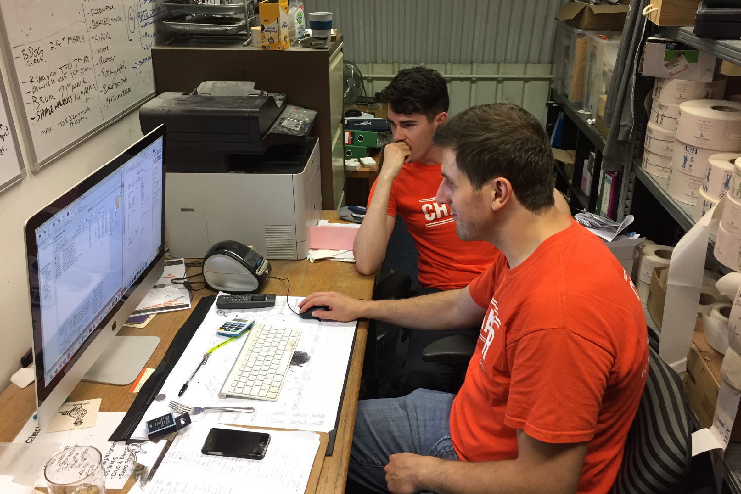 Two orange-shirted Chaser men looking at a computer screen in an industrial office