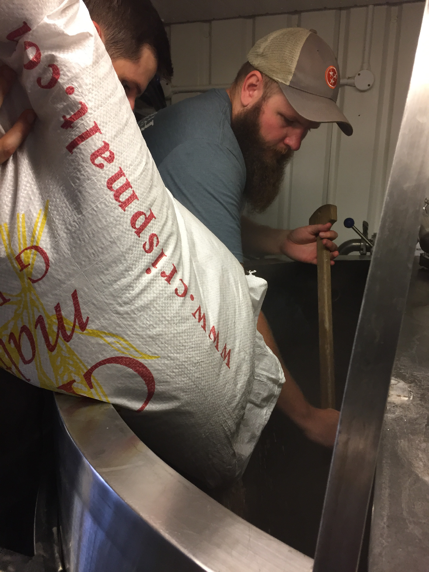 A heavily-bearded man mashing grain during a beer brew